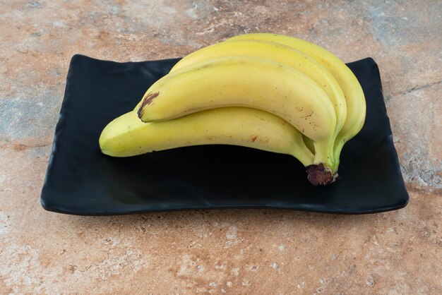 A dark plate full of ripe fruit bananas on gray table.