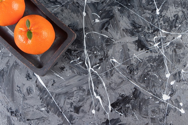 Free photo dark plate of juicy whole and sliced oranges on marble surface