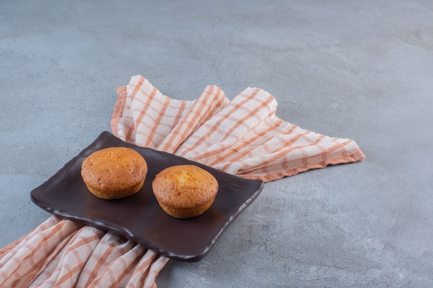 Dark plate of mini sweet cakes on stone table.