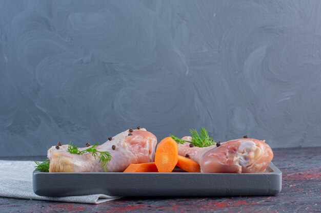 Dark plate of raw chicken drumsticks on marble surface