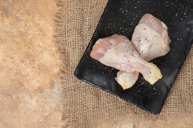 Free photo a dark plate of uncooked chicken legs with spices on sackcloth
