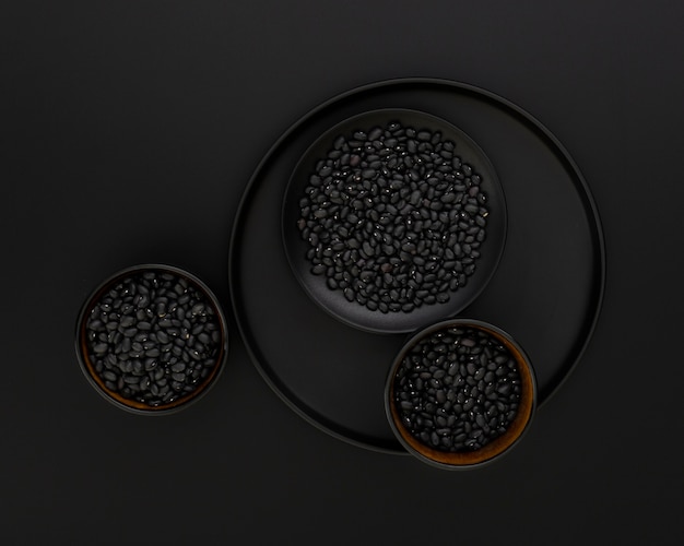 Dark plate with black bowls of beans on a black background