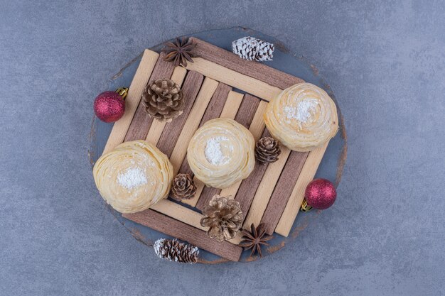 Un piatto scuro con biscotti e pigne di natale