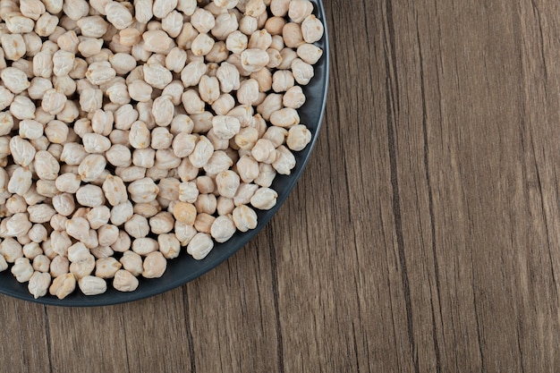 Free photo a dark plate with unprepared white peas on a wooden table