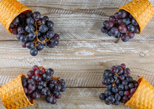 Темно-красный виноград в плетеных корзинах на деревянных фоне, плоская кладка.