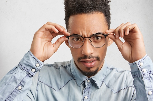 L'uomo afroamericano dalla pelle scura sembra rigoroso attraverso gli occhiali, indossa una camicia di jeans