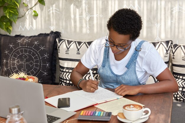 Dark skinned girl with short hairstyle, dressed in white t shirt and jean sarafan