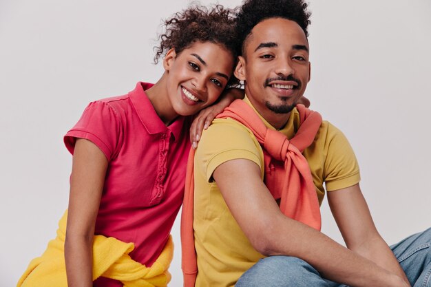 Dark-skinned guy and girl sitting on white wall