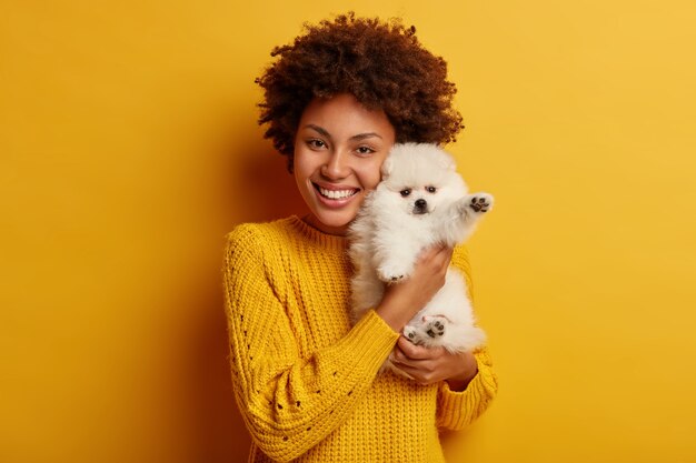 dark skinned lady keeps lips rounded, wants to kiss adorable pet, plays with small puppy