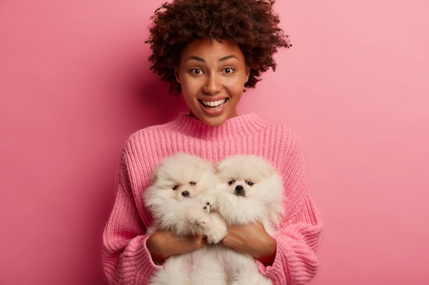 dark skinned lady keeps lips rounded, wants to kiss adorable pet, plays with small puppy