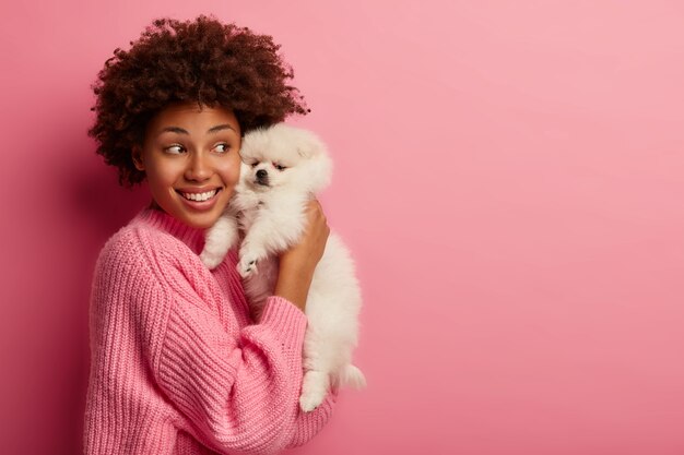 dark skinned lady keeps lips rounded, wants to kiss adorable pet, plays with small puppy