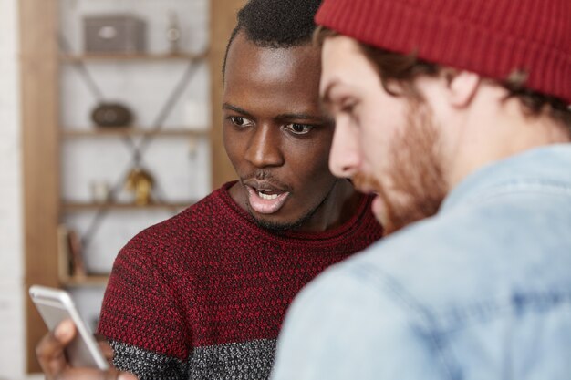 Dark-skinned man and his Caucasian bearded hipster surfing internet on cell phone