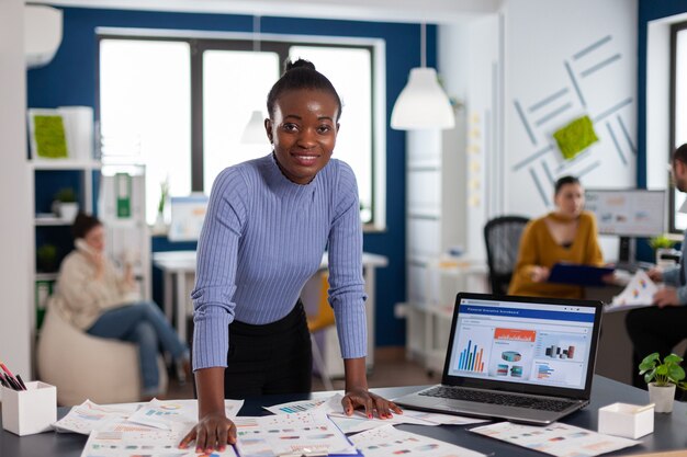 Темнокожая женщина и коллеги по корпоративному запуску офиса работают над завершением проекта. Разнообразная команда деловых людей, анализирующих финансовые отчеты компании с компьютера.