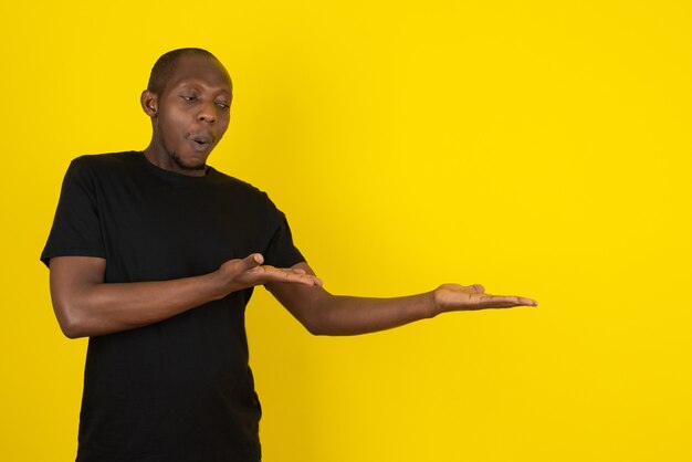 Dark-skinned young man showing something on yellow wall