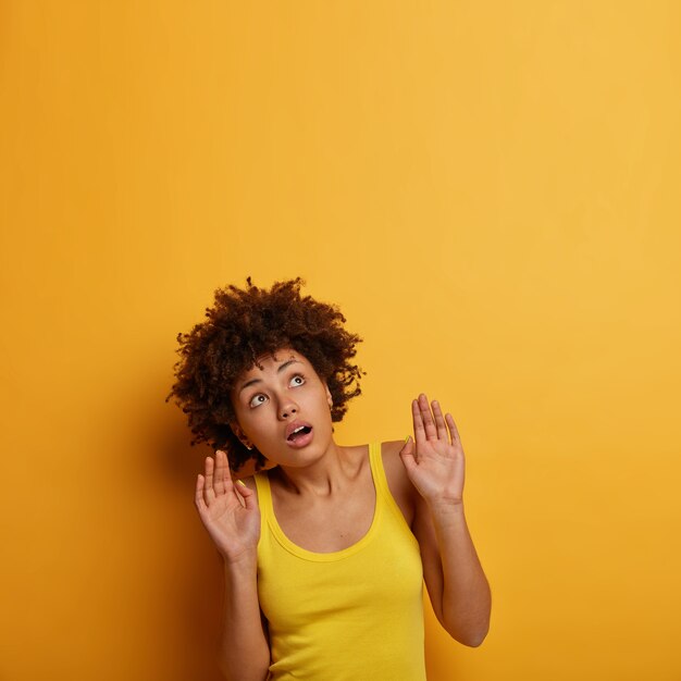 Dark skinned young woman afraid of something above her, looks upwards with scared expression