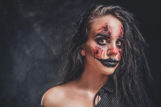 In the dark, smoky photo studio young girl has a photo shoot in a role of creepy clown.