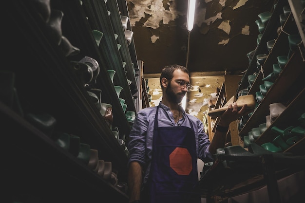 In the dark storage shoemaker in glasses is trying to find right shoe form.