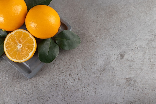 Dark wooden board of fresh juicy oranges on stone table.