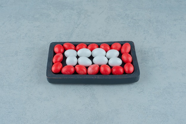 A dark wooden board full of round sweet colorful candies on white surface