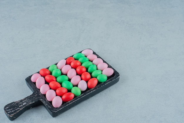 A dark wooden board full of round sweet colorful candies on white surface