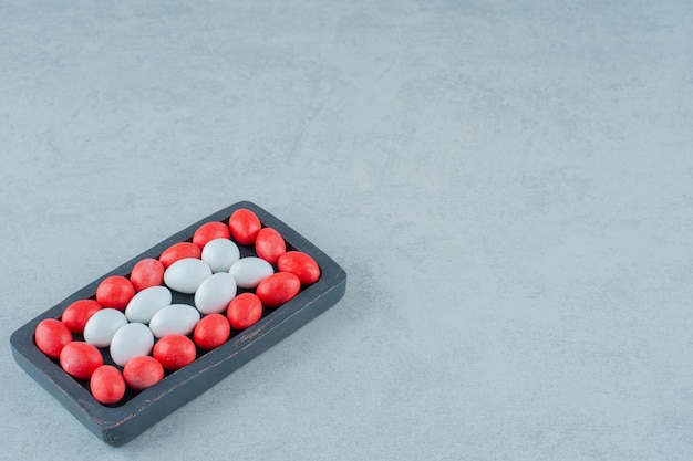 A dark wooden board full of round sweet colorful candies on white surface