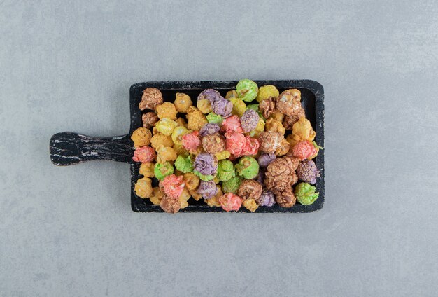 A dark wooden board full of sweet multicolored popcorn .  