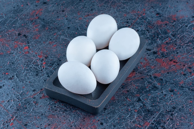 生の白い鶏の卵が入った暗い木の板。