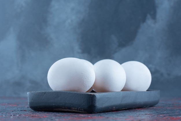 A dark wooden board with raw white chicken eggs 