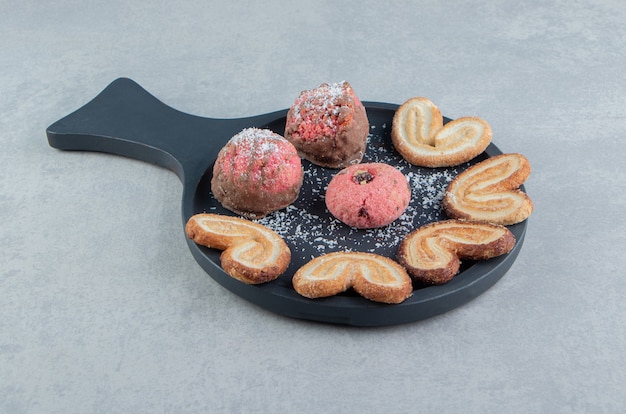 A dark wooden board with sweet cookies with sugar powder. 