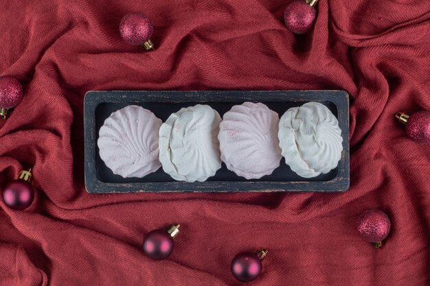 A dark wooden board with vanilla and pink zephyrs with Christmas balls.