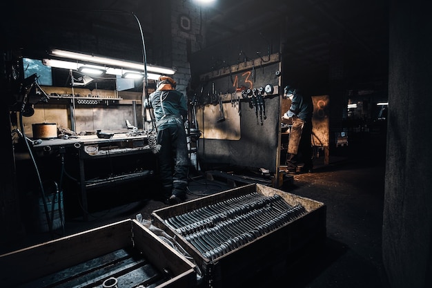 暗いワークショップでは、保護服を着た経験豊富な労働者が金属を扱っています。