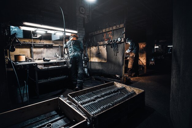 At the dark workshop experienced worker in protective uniform is working with metal.