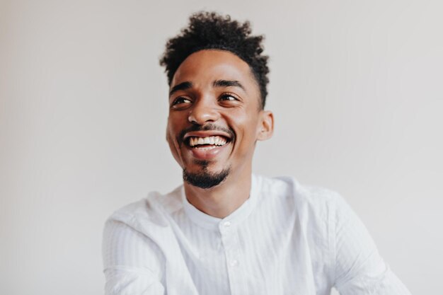 Darkskinned guy in white shirt laughs on isolated background Charming man in great mood smiling on white backdrop