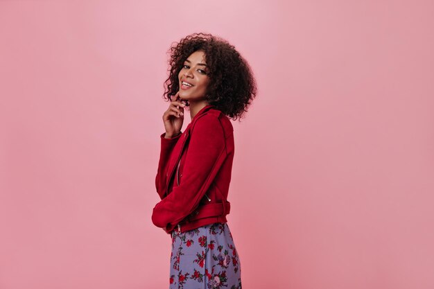 Darkskinned woman crossed her fingers on pink background Pretty girl in red jacket and floral dress posing on isolated backdrop