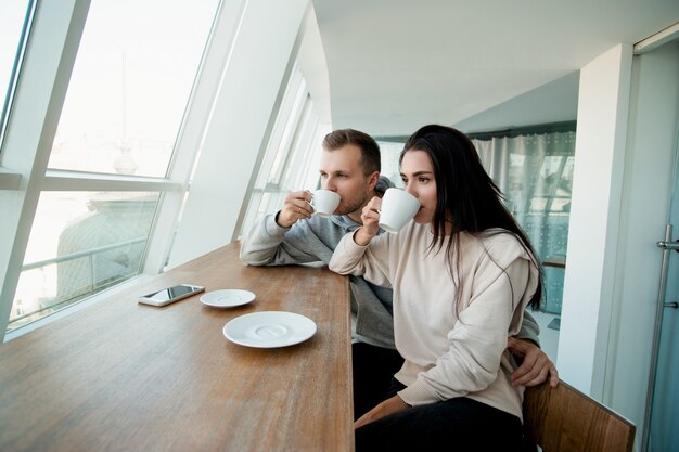 温かい飲み物を飲む若いカップル テーブルの上に暖かいコーヒーのカップを持って カフェに座っている女性と男性を閉じます 居心地の良い喫茶店で週末を一緒に過ごす男女 ロマンチックな日付の概念 プレミアム写真