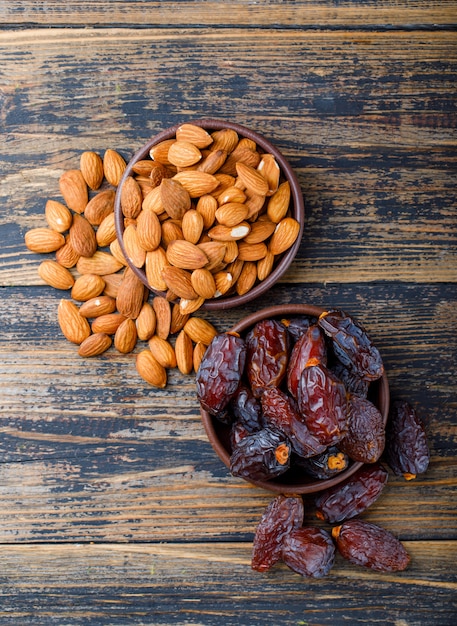 Dates and almonds in clay plates on wooden background, top view.