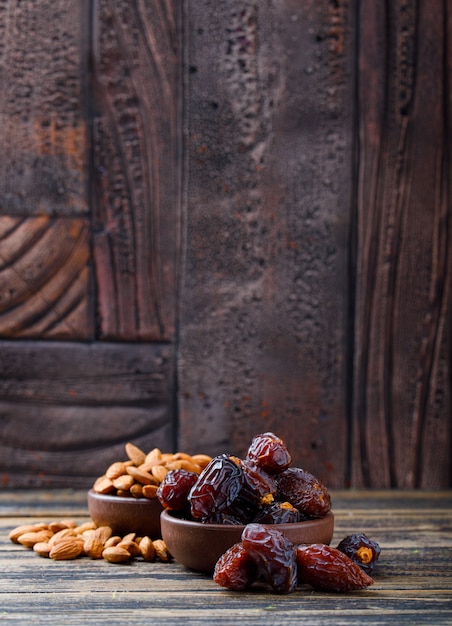 Free photo dates and almonds in clay plates on wooden and stone tile background. side view.