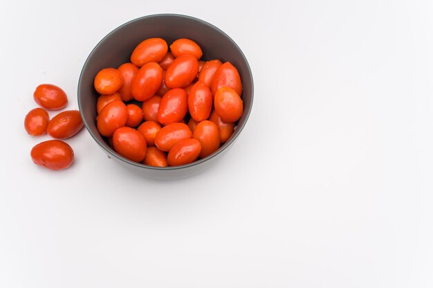 Datterini tomatoes in a dark stoneware bowl on a white backgroun