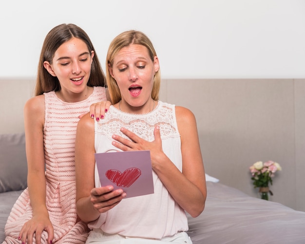 Daughter and amazed mother reading greeting card 