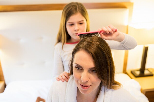 Daughter combing her mothers hair in bedroom