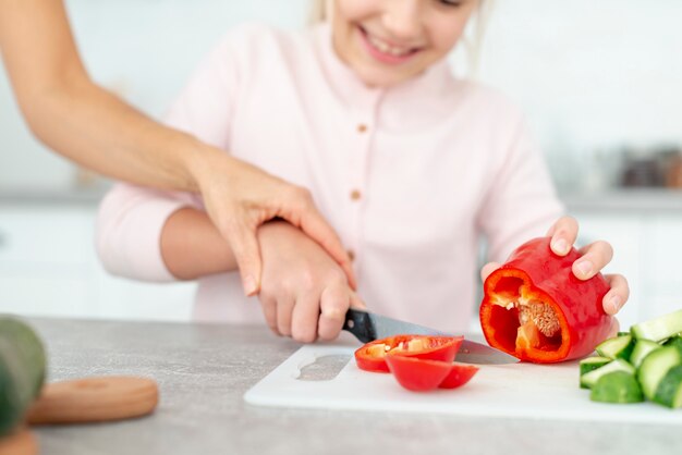 daughter cutting peppers helped by her mother