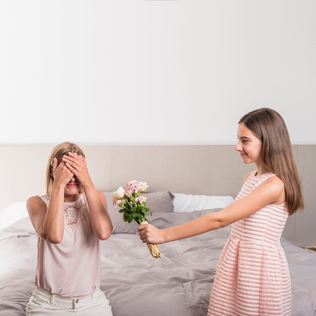 Daughter giving flowers bouquet to mother in bedroom 