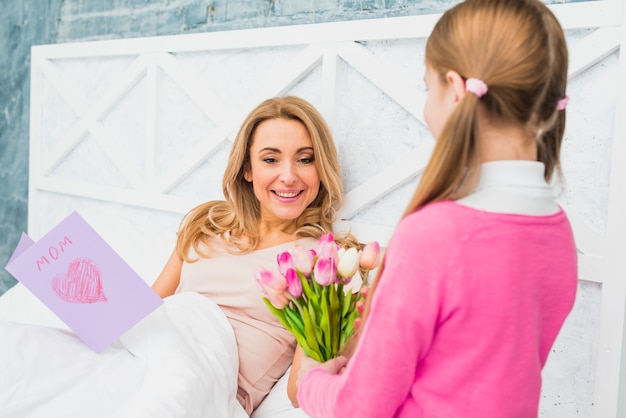 Daughter giving tulips to mother in bed 