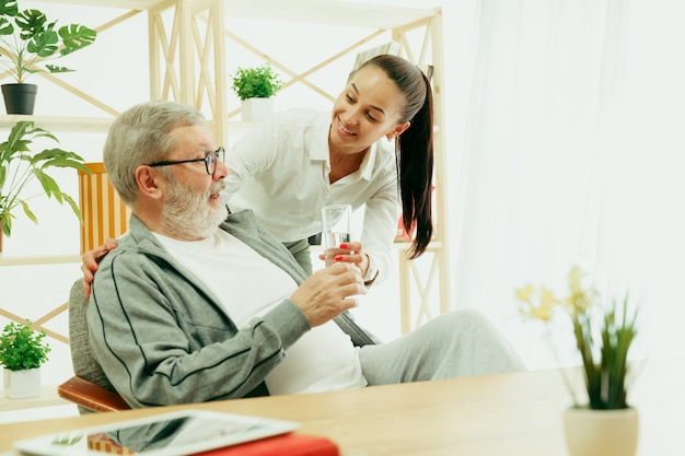 Una figlia o una nipote trascorre del tempo con l'acqua potabile del nonno o dell'uomo anziano. famiglia o festa del papà, emozioni e felicità. ritratto di stile di vita a casa. ragazza che si prende cura di papà.