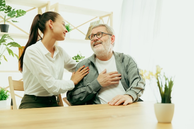 A daughter or granddaughter spends time with the grandfather or senior man. Family or fathers' day, positive emotions and happieness. Lifestyle portrait at home. Girl taking care about dad.