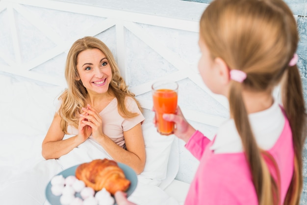 Daughter holding croissant and juice for mother in bed 