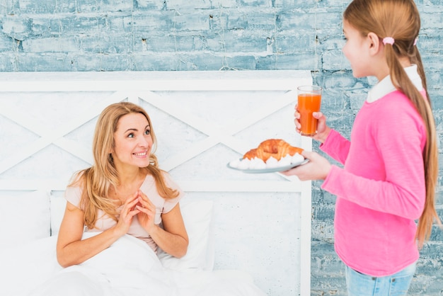 Daughter holding croissant on plate for mother in bed 