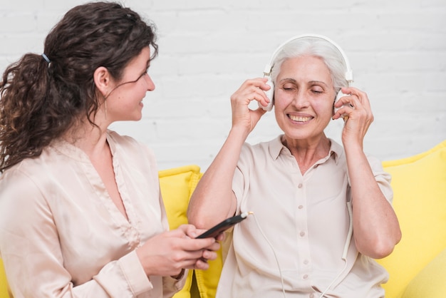 Free photo daughter holding mobile phone while her mother listening music on headphone