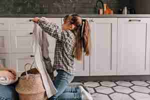 Foto gratuita la figlia in jeans e camicia aiuta la mamma e tira fuori i vestiti sporchi dal cestino.