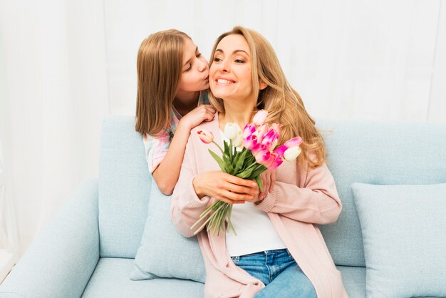 Daughter kissing happy mother with flowers